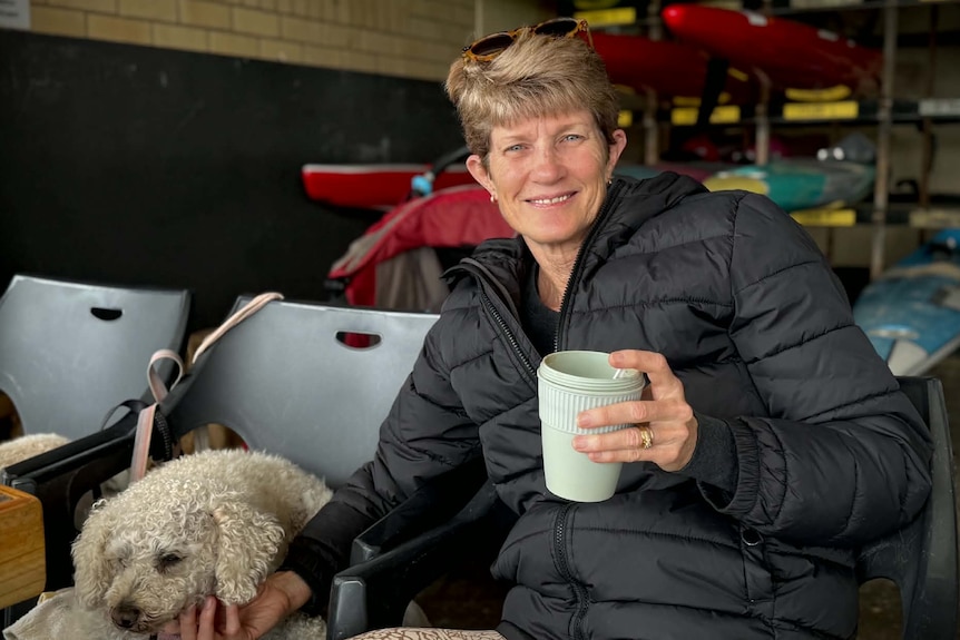 A woman with a takeaway coffee in her hand and patting a dog.