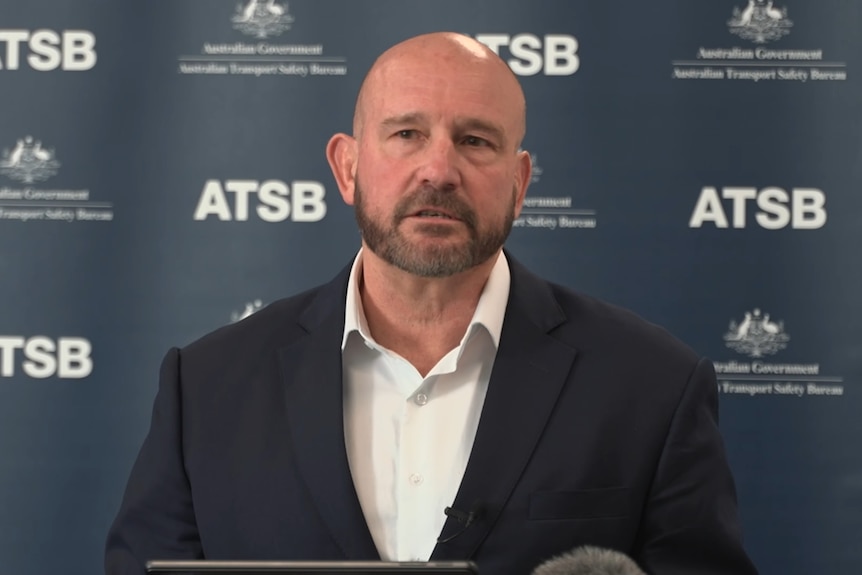 A bald man in a suit addressing press. 
